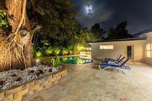 Ein Schwimmbad mit Liegestühlen, einem Baum und einem Gebäude mit beleuchteter Fassade.