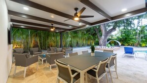 An outdoor patio with a dining table, chairs, and a ceiling fan. - Villa Azur by Glam Homes (North Miami Beach)