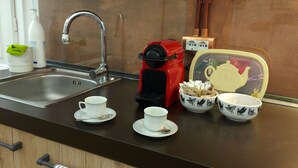 En köksbänk med ett handfat, en röd kaffebryggare, två vita koppar och en tekanna med fågelmotiv.