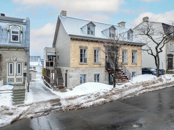 A two-story residential building with a brick facade, a visible staircase, and a snow-covered ground.
