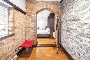 A narrow hallway with a brick wall, a wooden floor, and a red bench.