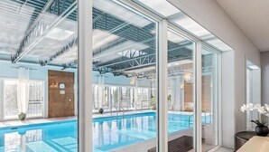 Un espace piscine intérieur moderne avec des murs en verre, un mur en bois et un banc.