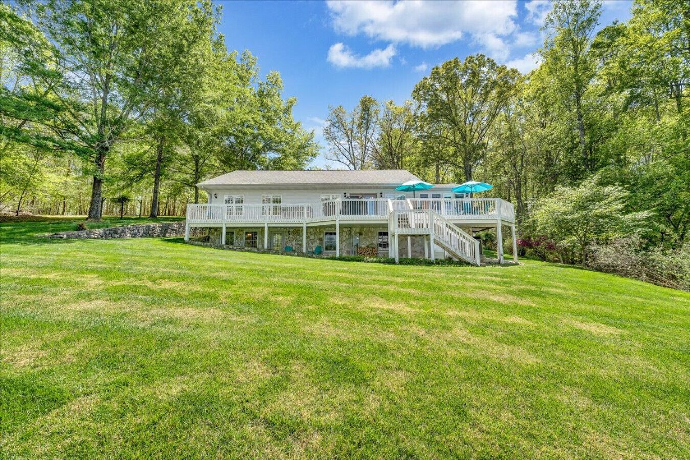 A large house with a spacious deck, surrounded by a well-maintained lawn and trees.