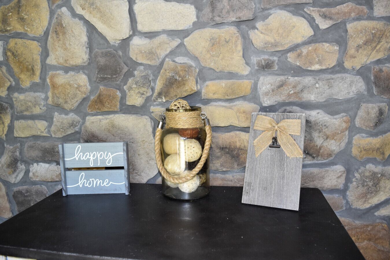 A stone wall, a jar with a rope, a sign saying 'happy home,' and a wooden box with a bow.