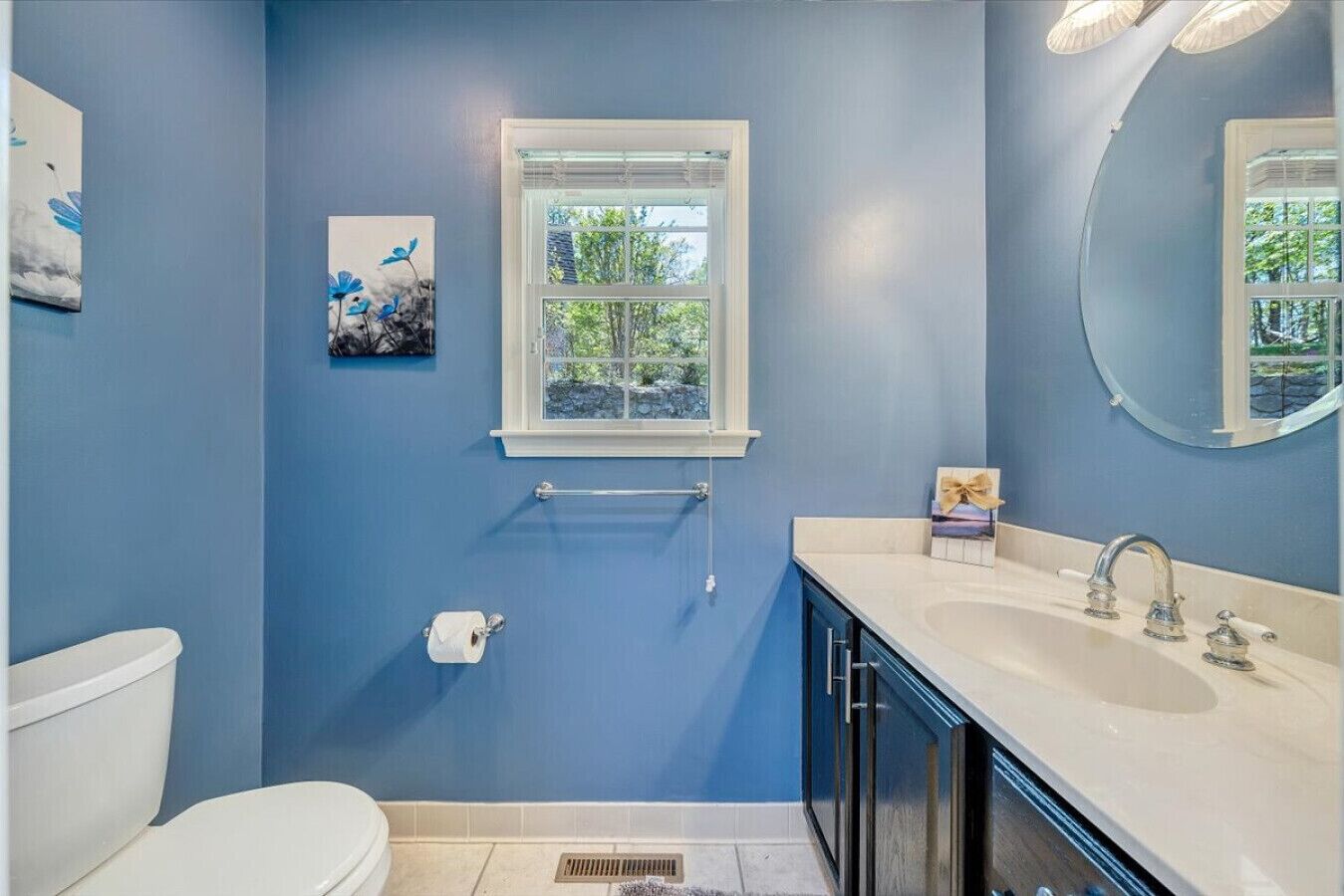 A bathroom with a blue wall, a window, a toilet, a sink, and a mirror.