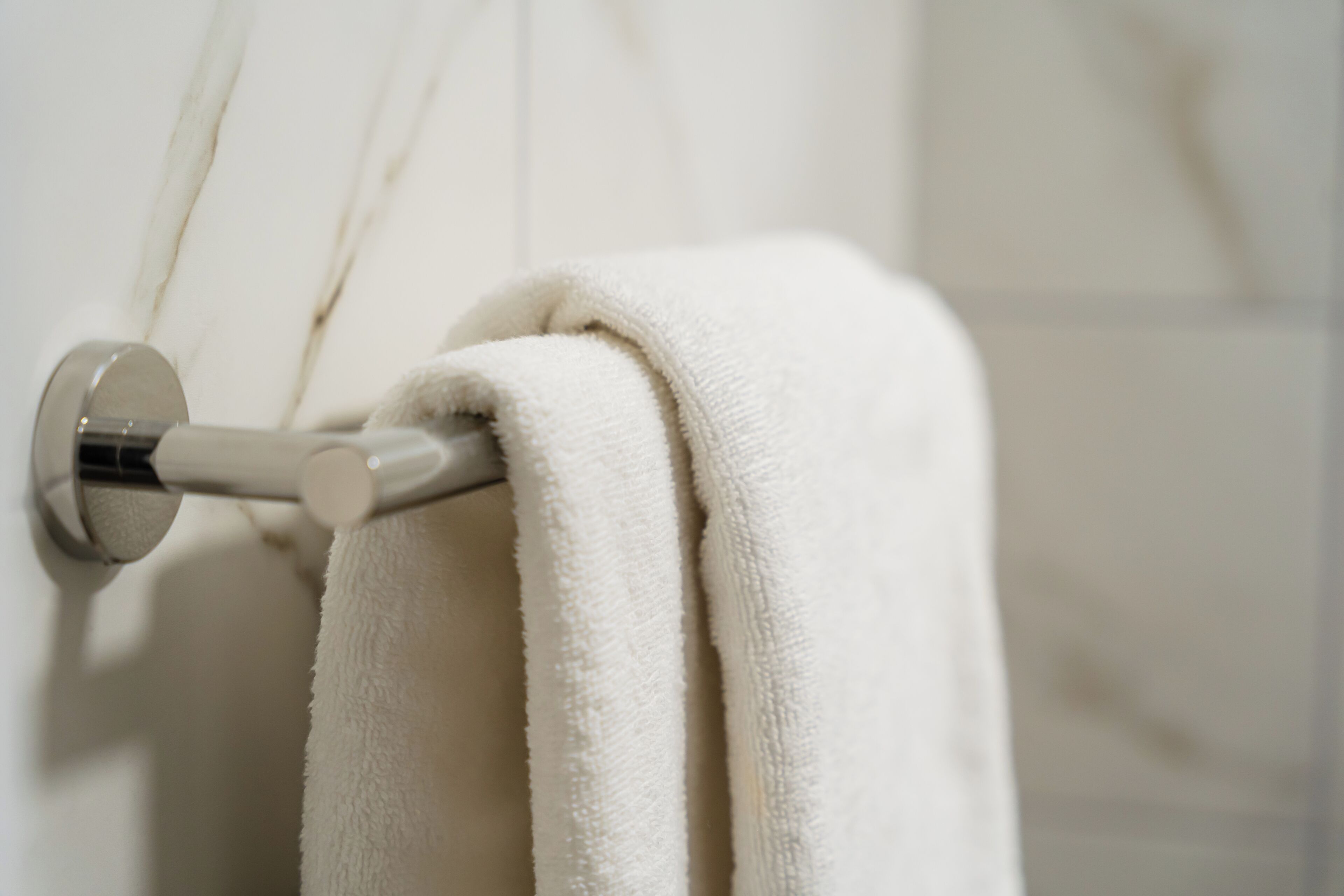 A white towel hanging on a metallic towel rack in a bathroom.