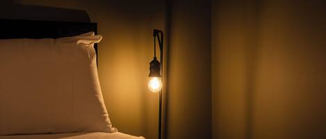 A bed with white bedding, a nightstand with a lamp, and a wall with a curtain.