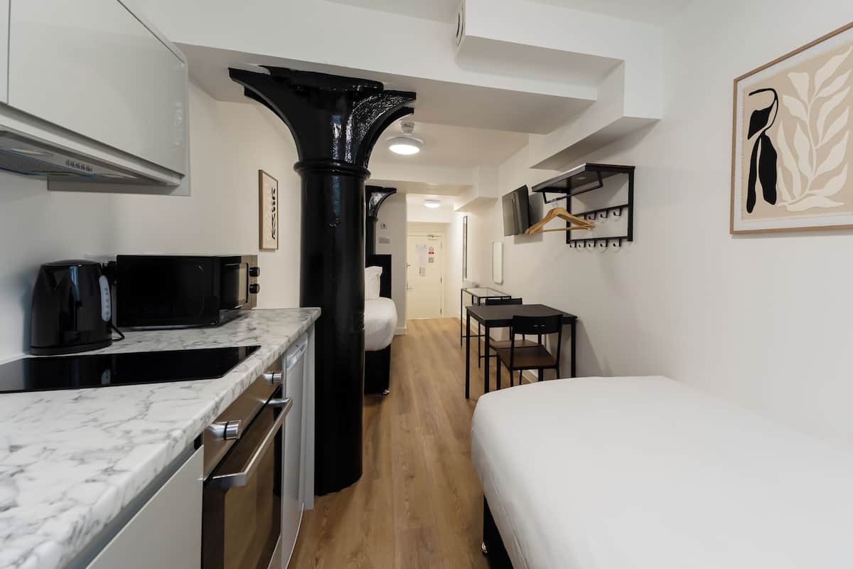 Une chambre d’hôtel de taille réduite, équipée d’une kitchenette, d’un lit, d’un bureau et d’une chaise.