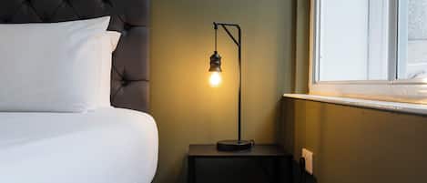 A bed with a tufted headboard, a bedside table with a lamp, and a window with a view.