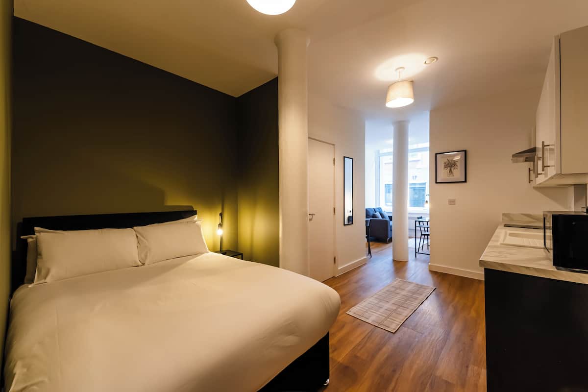 Une chambre à coucher comprenant un lit, des tables de chevet, une commode, un bureau, une chaise et donnant sur le salon.