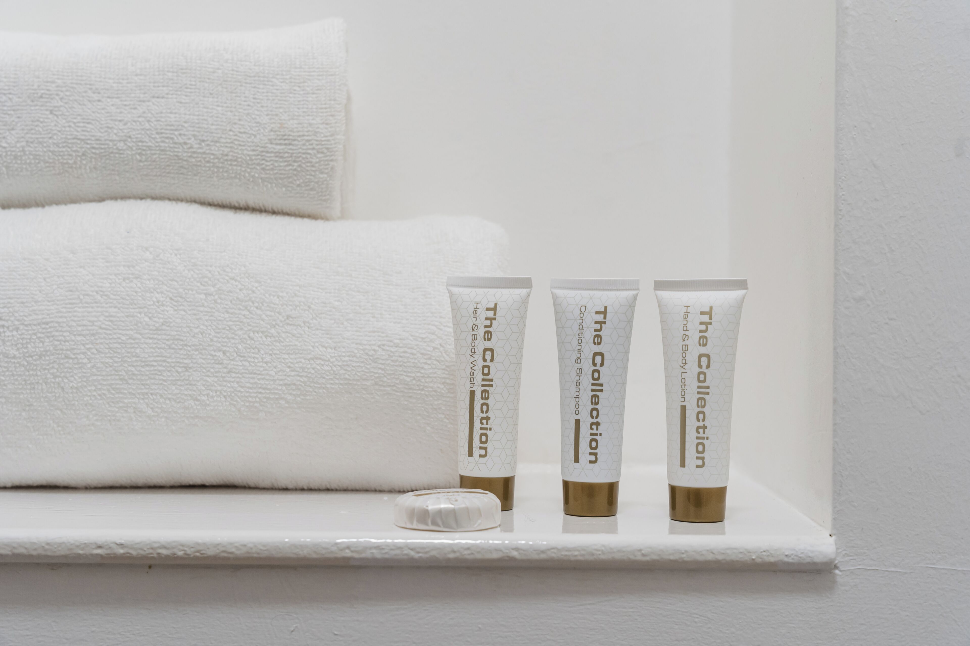 A shelf with three toiletry tubes labeled 'The Collection' and a white towel.
