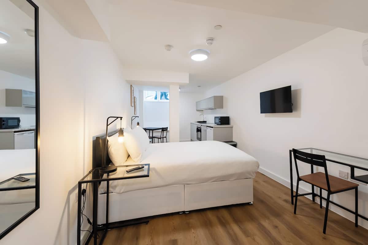 Une chambre d’hôtel moderne équipée d’un lit, d’une table de chevet, d’une chaise et d’un téléviseur fixé au mur.