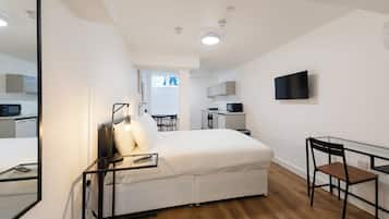 Een moderne hotelkamer met een bed, nachtkastje, stoel en een aan de muur bevestigde televisie.