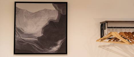 A framed abstract artwork on a wall, a wooden coat rack with hangers, and a white wall.