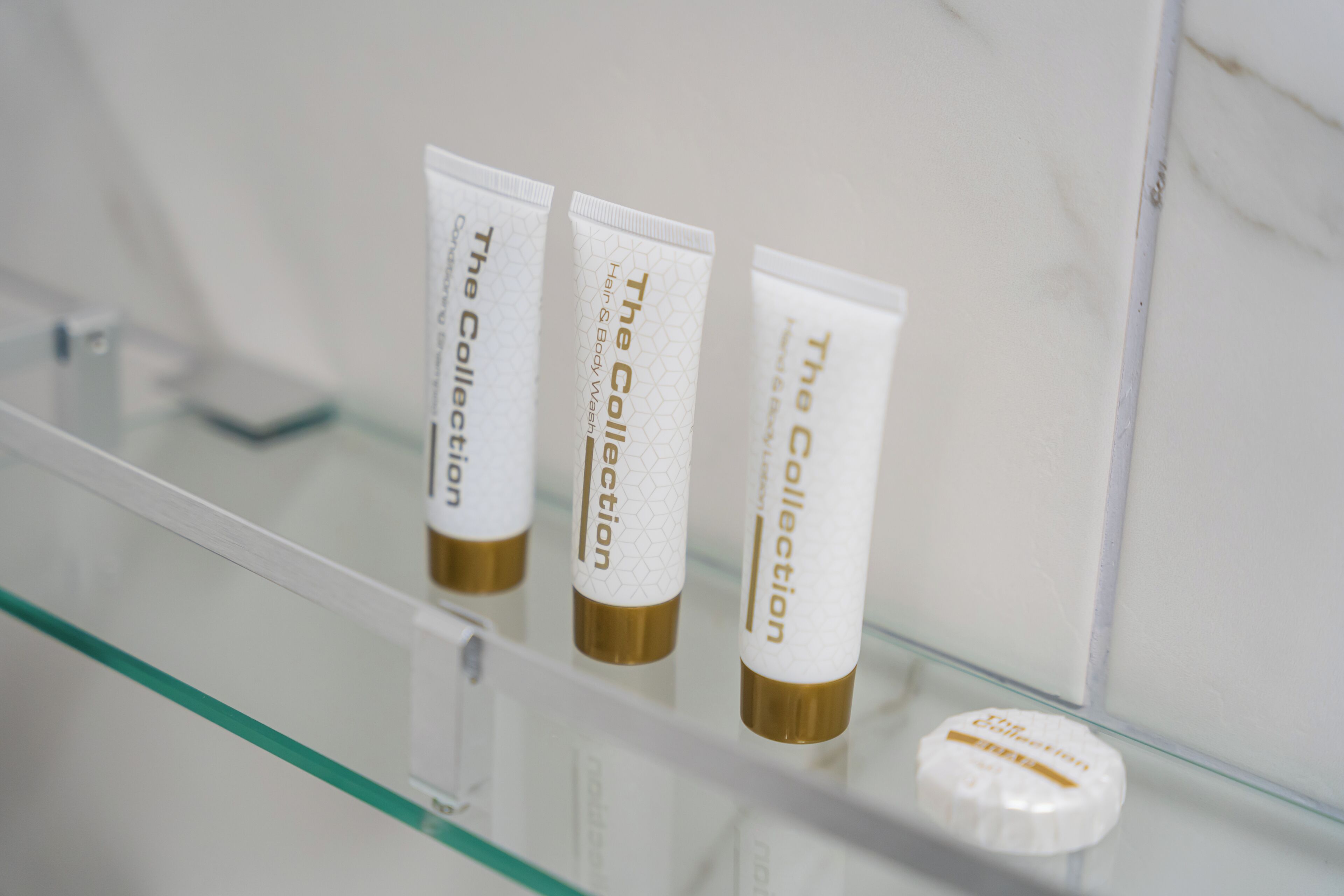 Three white tubes with gold caps labeled 'The Collection' on a glass shelf.