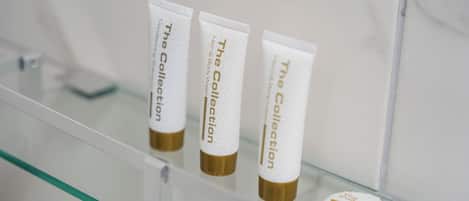 Three white tubes with gold caps labeled 'The Collection' on a glass shelf.