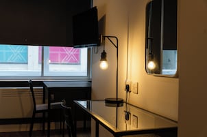 Una cocina moderna con una mesa de vidrio, sillas negras, un televisor montado y una lámpara fijada a la pared.