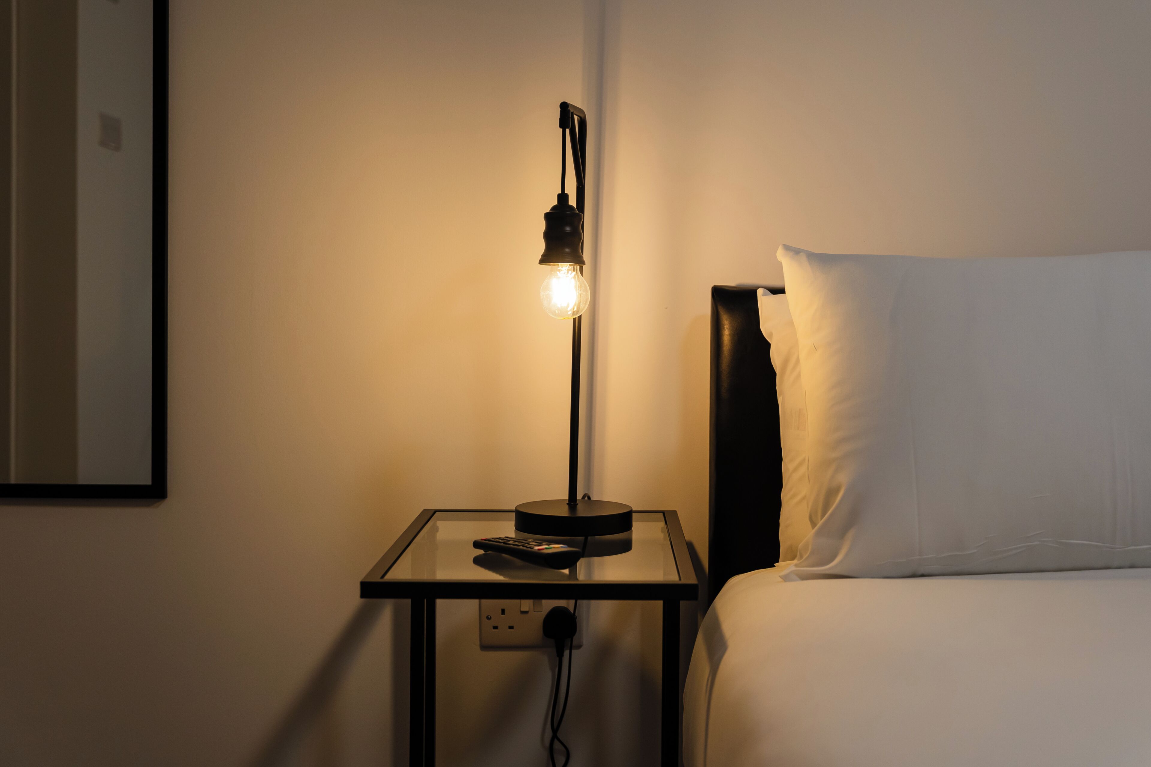 Un comodino con una lampada, un telecomando e una presa elettrica.