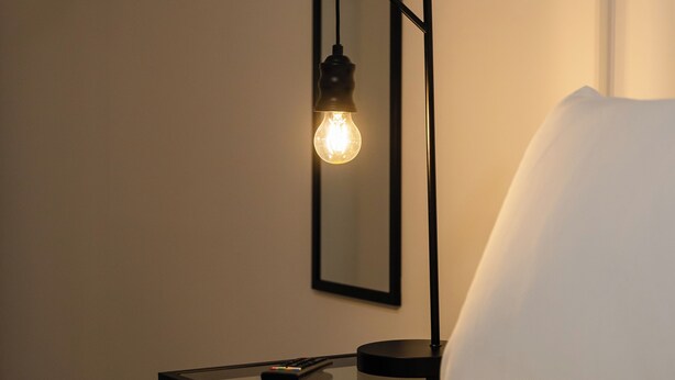 A bed with a white pillow, a bedside table with a lamp, and a wall-mounted mirror. - 8 Stanley Street (Liverpool)