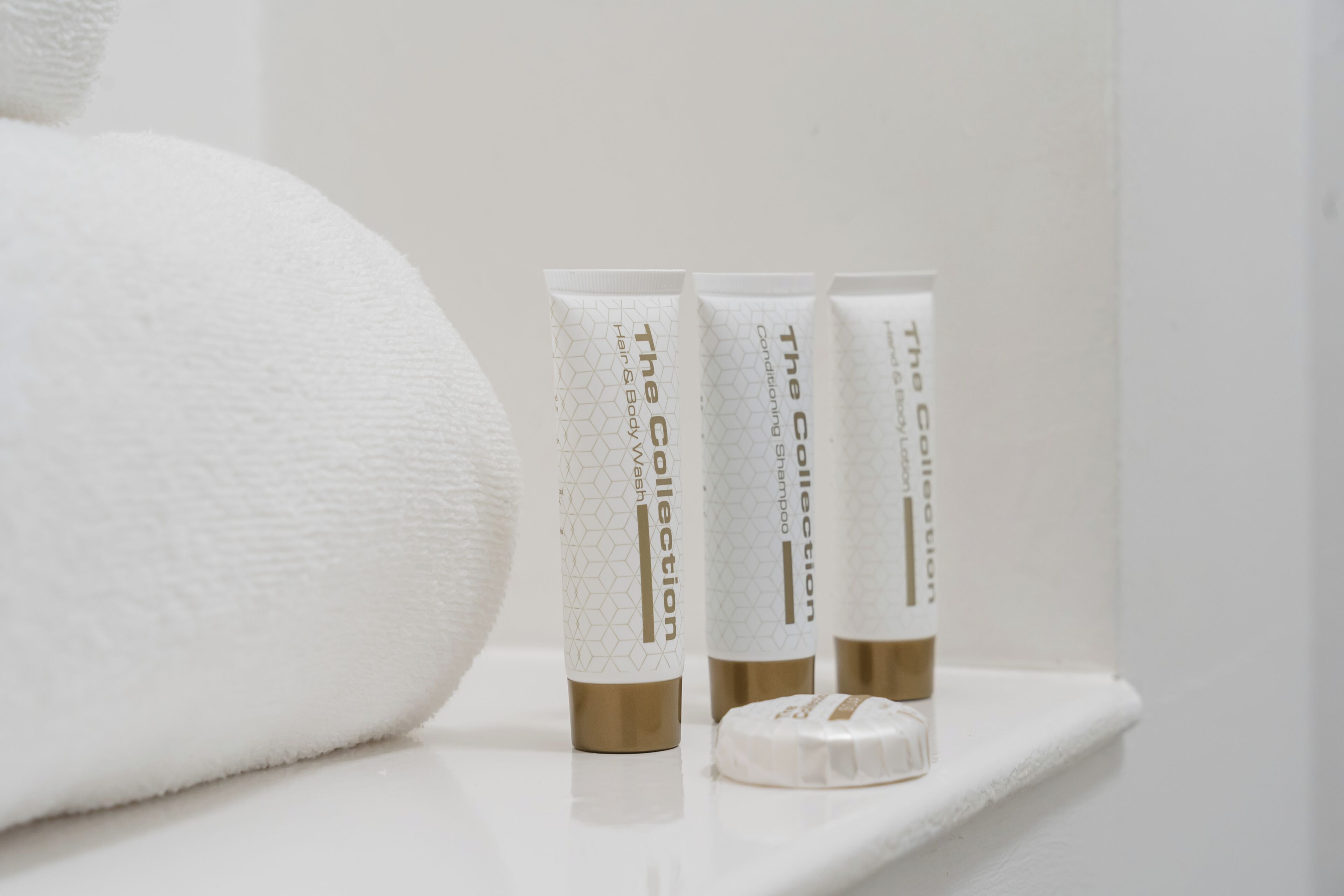A white towel and three toiletry bottles on a white shelf.