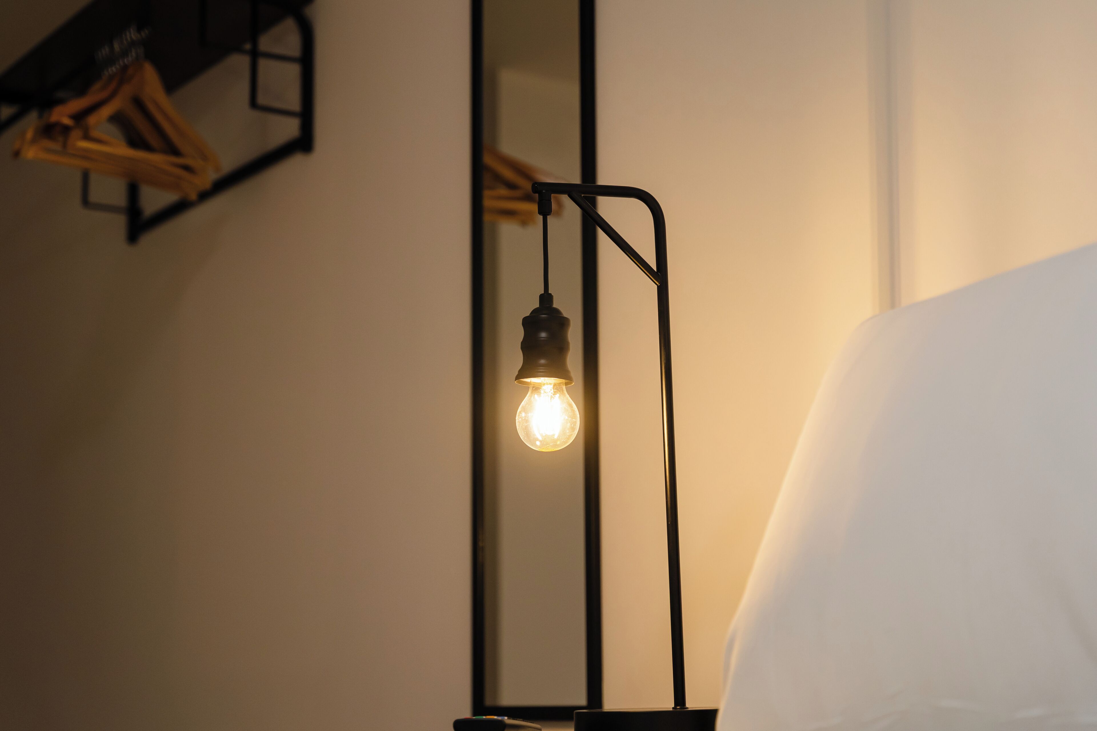 Ein Zimmer mit einem Bett, einem wandmontierten Spiegel und einer Stehlampe mit Glühbirne.