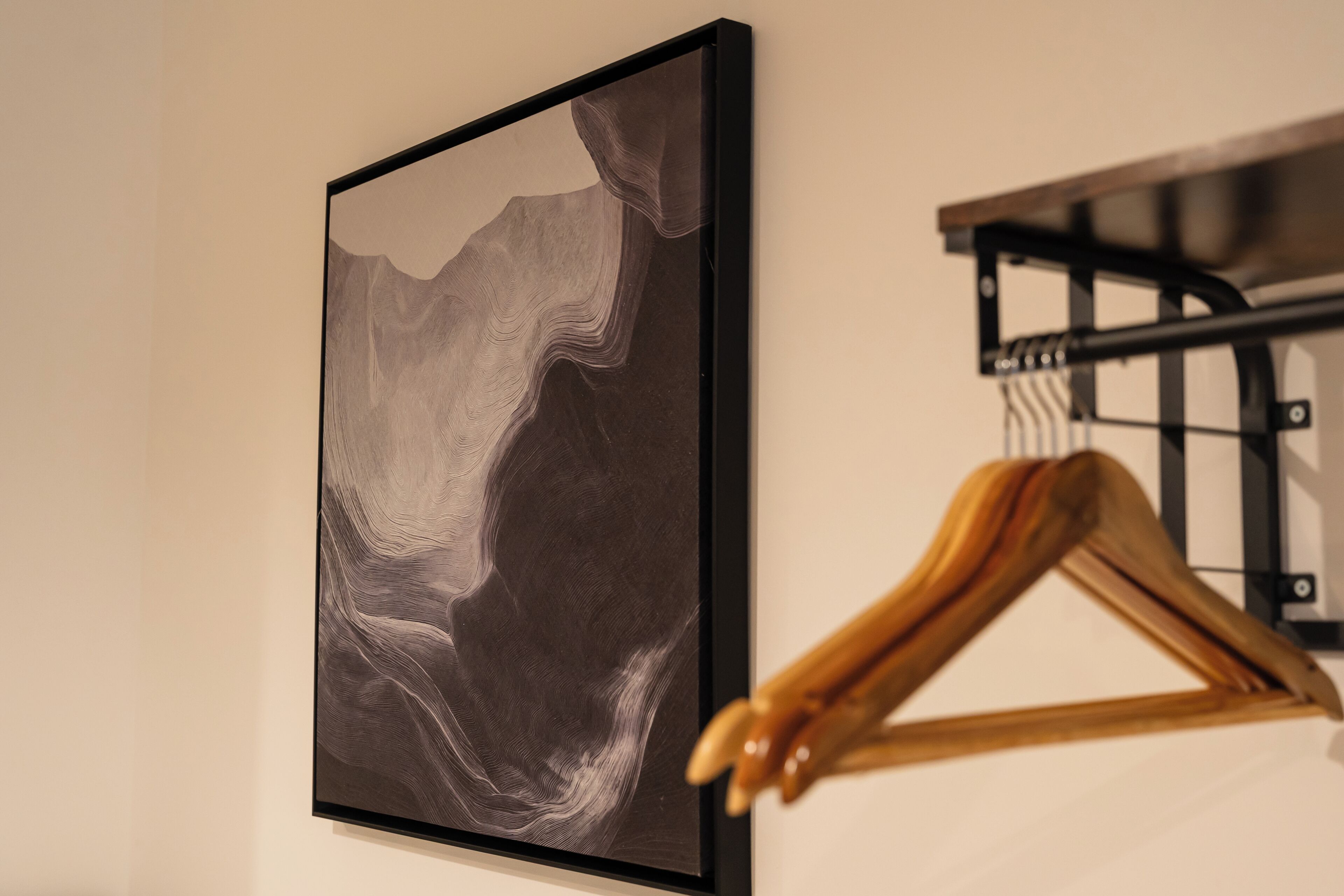 Una obra de arte abstracta en un marco colgada en una pared, un perchero de madera y una estantería de metal negro.