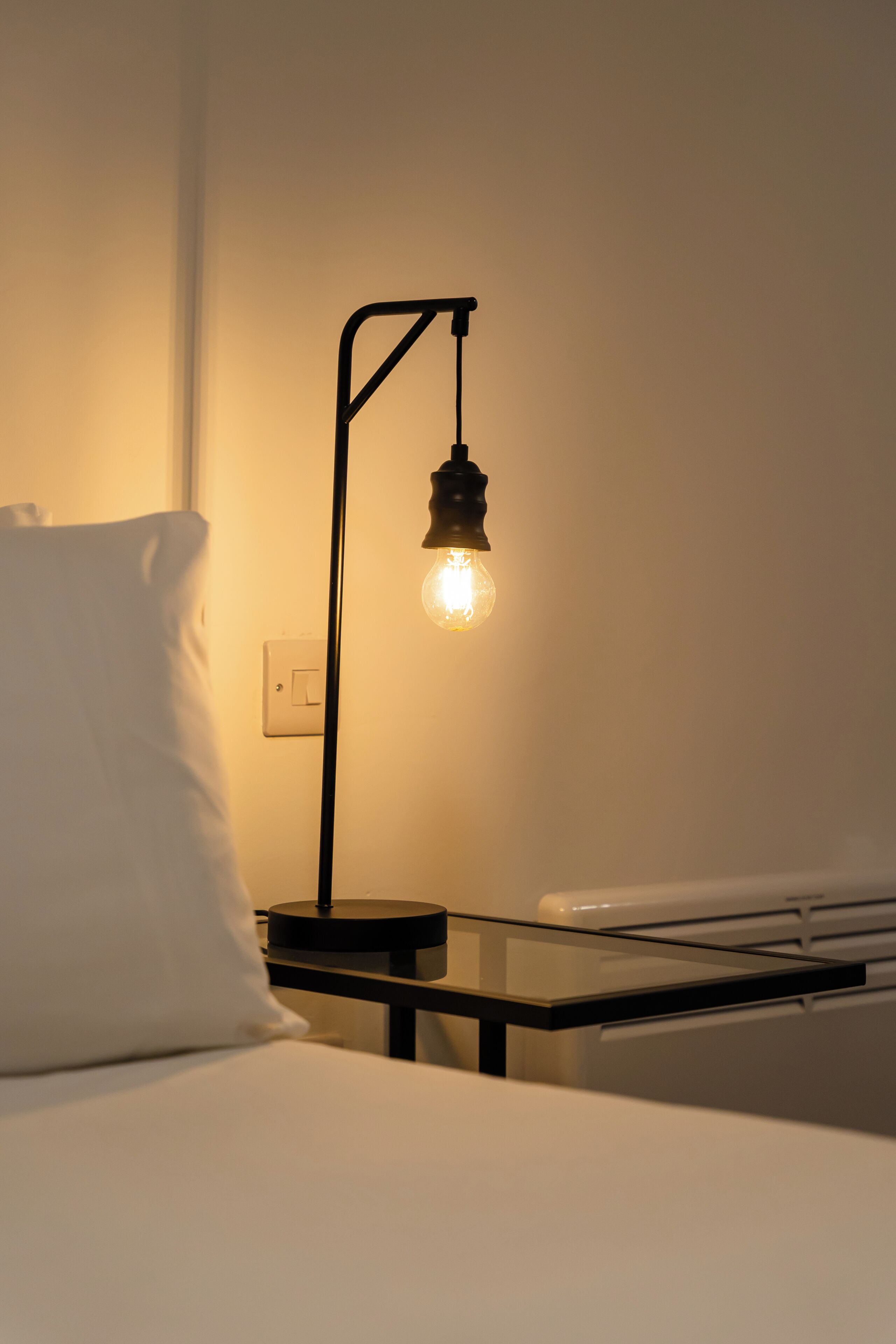 A bed with a white pillow and a bedside table with a lamp.