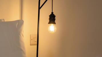 Ein Bett mit weißem Kopfkissen und einem Nachttisch mit Lampe.