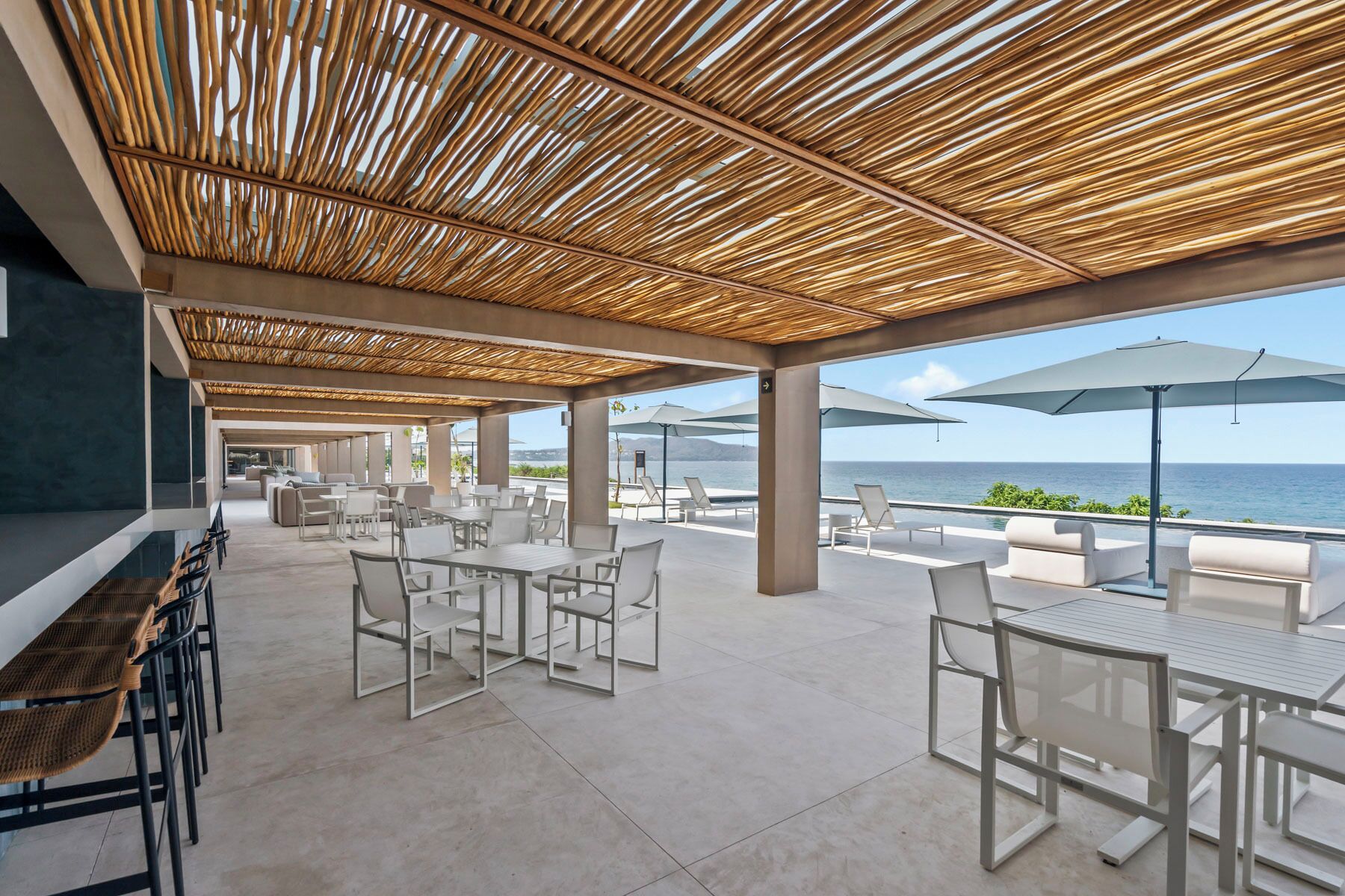Un patio al aire libre con mesas, sillas, una parrilla y sombrillas, con vista al mar.