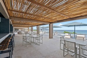 Un patio al aire libre con mesas, sillas, una parrilla y sombrillas, con vista al mar.