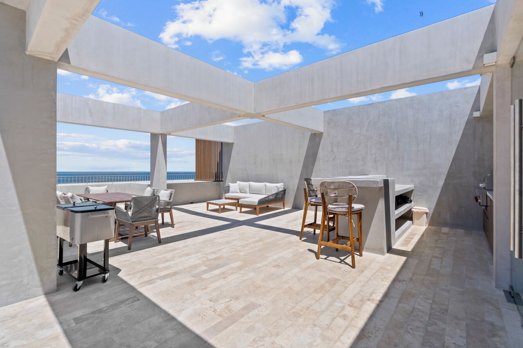 A spacious outdoor deck with a view of the ocean, featuring a dining area, seating, and a grill.