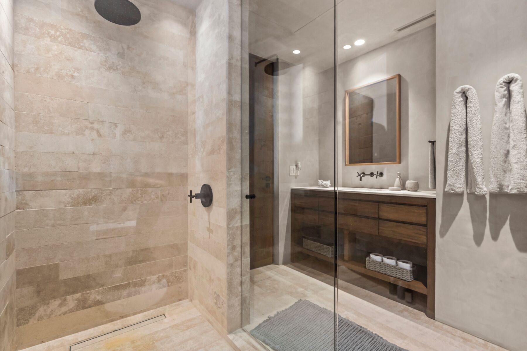 Un baño moderno con ducha de vidrio, tocador de madera y un espejo grande.