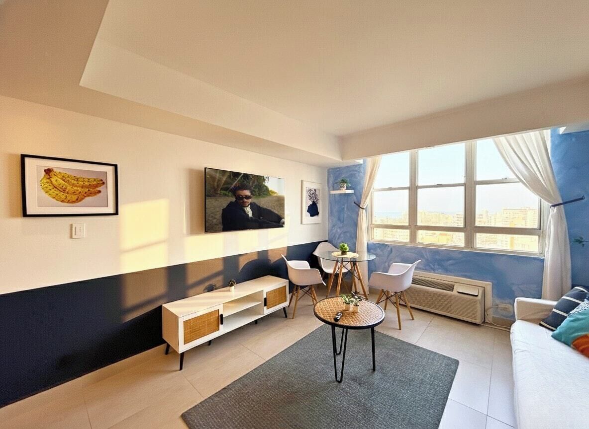 Un salon moderne avec un canapé, une table à manger et des chaises, un téléviseur et des œuvres d’art accrochées au mur.