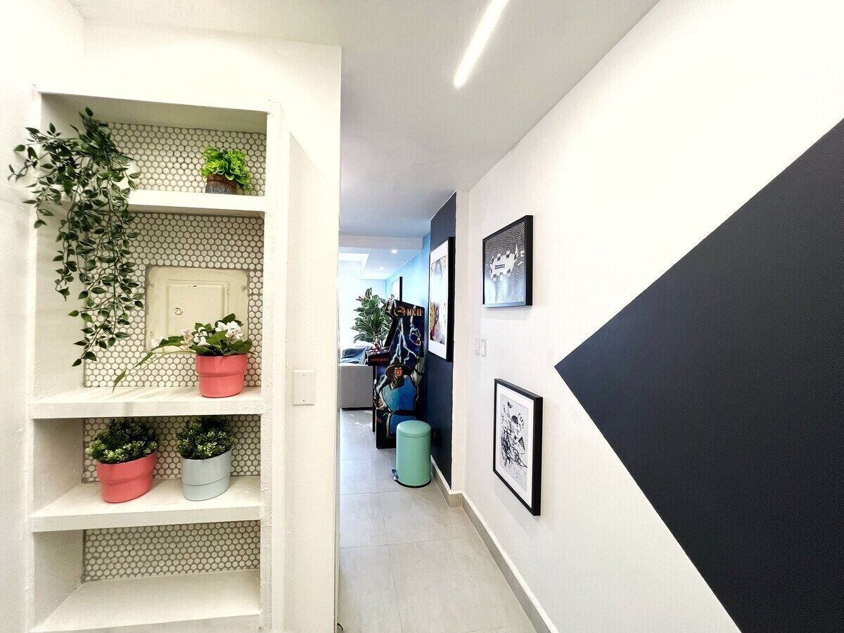 Un couloir avec une étagère blanche où sont disposées des plantes en pot, un mur d’accent noir et des œuvres d’art encadrées.