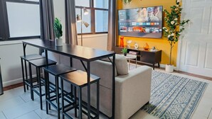En moderne stue med en sofa, et spisebord med stole, et fjernsyn ophængt på væggen og en potteplante.