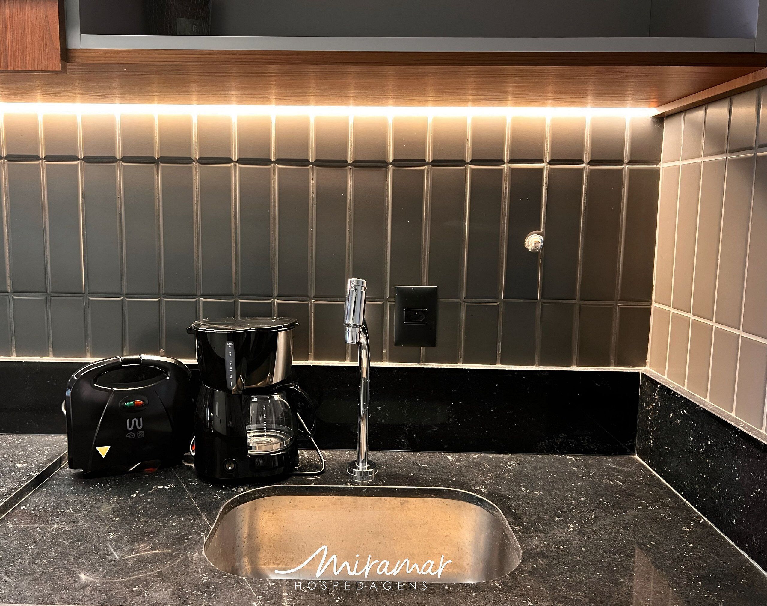 A modern kitchen with a coffee maker, a sink, and a wall-mounted light.