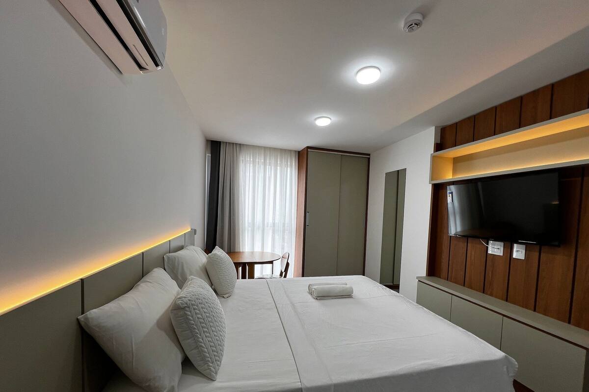 Una habitación de hotel con cama, televisión, escritorio y ventana con cortinas.