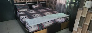 A bed with patterned bedding, a bedside table, and a window with curtains. - Regard Confidential Hotel & Suites (Lagos)