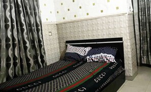 A single bed with a patterned bedspread, a headboard, and a pillow with a checkered design. - Regard Confidential Hotel & Suites (Lagos)