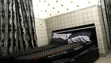 Una cama con estructura negra y ropa de cama estampada, cortina con diseño y pared con textura y motivos geométricos.
