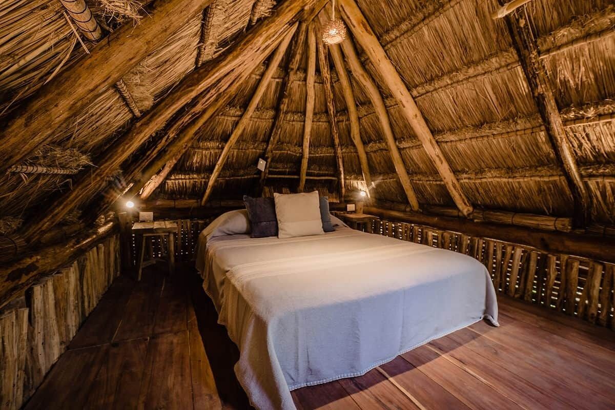 A thatched-roof room with a bed, wooden walls, and a small table.