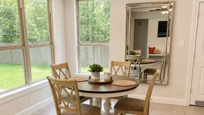 Ein Essbereich mit einem runden Tisch, vier Holzsesseln, einem Blumentopf und einem Spiegel an der Wand.