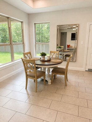 A dining area with a round table, four wooden chairs, a potted plant, and a mirror on the wall.