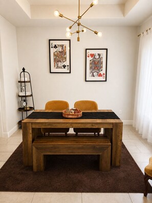 A dining area with a wooden table, two chairs, a bench, a chandelier, and two framed artworks on the wall.