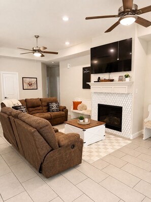 A living room with a sofa, a coffee table, a fireplace, and a TV mounted on the wall.