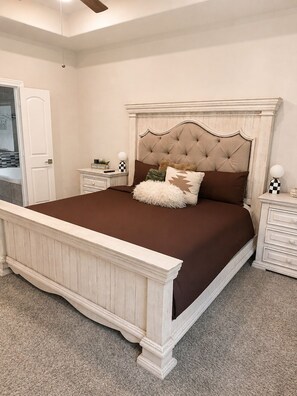 A bedroom with a large bed, two bedside tables, a nightstand, and a door leading to a bathroom.