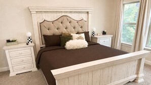 Ein Schlafzimmer mit einer gepolsterten Kopfteil, einem großen Bett, zwei Nachttischen und einem Fenster mit Vorhängen.