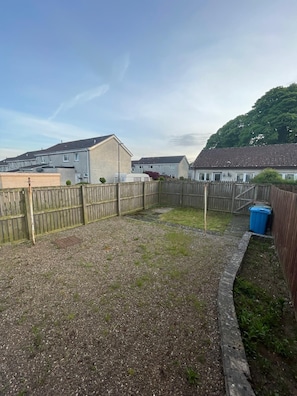 A residential backyard with a gravel area, a wooden fence, and houses in the background.