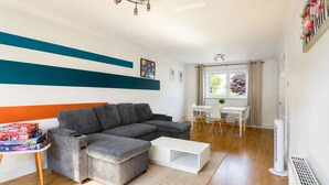 Un salon moderne avec un canapé d’angle, une table basse blanche et un coin repas comprenant une table et des chaises blanches.