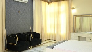 A hotel room with a bed, a seating area with chairs, a ceiling fan, an air conditioning unit, and a chandelier. - The Most Luxurious Private Resort in Karachi (Karachi)